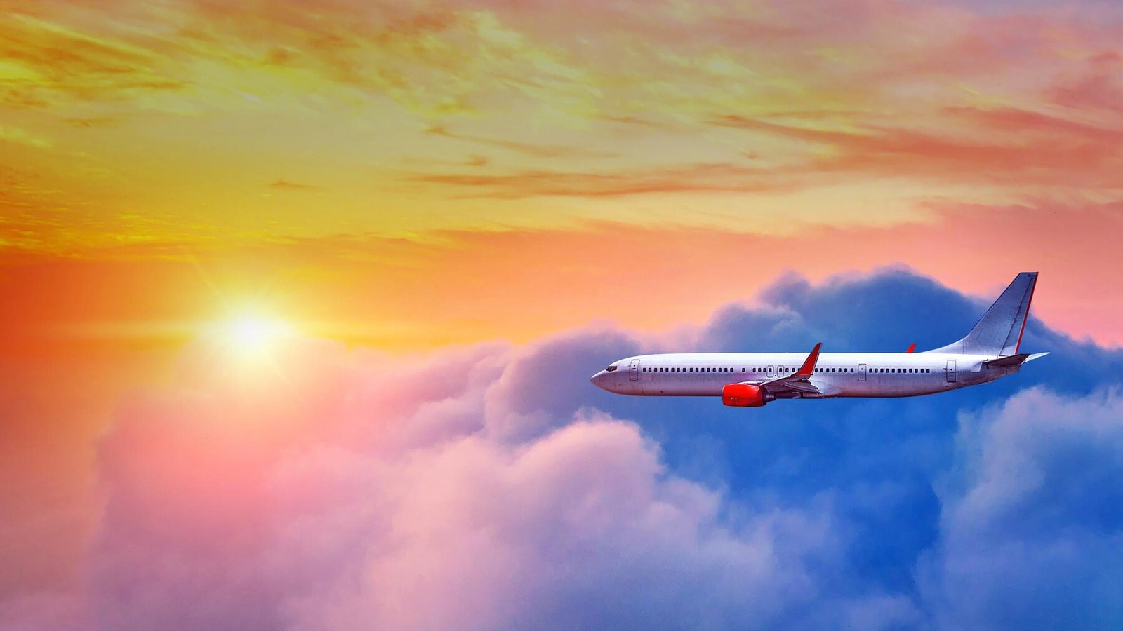 Airplane flying over clouds during sunset